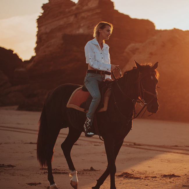 woman riding a horse and wearing a white crop top pattern and jeans