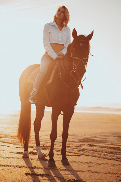 woman riding a horse wearing a white crop top and jeans